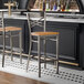 A metal bar stool with a cross back design and a natural wood seat.