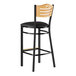 A Lancaster Table & Seating black wood bar stool with a black cushioned seat and natural wood back.