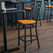 A Lancaster Table & Seating black cross back bar stool with a cherry wood seat.