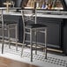 A Lancaster Table & Seating cross back bar stool with a detached black vinyl padded seat.