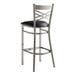 A metal bar stool with a cross back design and a black vinyl padded seat.