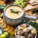 A Bon Chef stainless steel fondue pot with bread and fruit on a table.