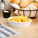 A Tuxton eggshell china oval baker filled with macaroni and cheese on a table with a basket of bread and silverware.