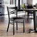 A black metal cross back chair with a black vinyl padded seat.