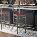 A metal bar stool with a cross back design and a mahogany wood seat.
