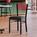 A Lancaster Table & Seating side chair with a black vinyl seat and mahogany wood back on a table in a restaurant dining area.