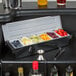 A Choice 6-compartment condiment bar on a counter with bowls of oranges and grapes.