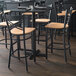 A black metal bar stool with a cross back design and a natural wood seat.