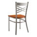 A Lancaster Table & Seating metal cross back chair with a wood seat.