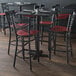 A Lancaster Table & Seating black cross back bar stool with a mahogany wood seat at a table in a restaurant.