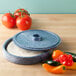 A blue round polyethylene tortilla server with a lid on a table with tortillas and peppers.