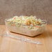 A clear deli crock filled with coleslaw with a clear plastic spoon.