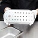 A person in gloves holding a stainless steel Vollrath false bottom with holes.
