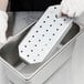 A gloved hand holding a Vollrath stainless steel steam table pan false bottom with holes.