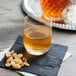 A Stolzle Weinland rocks glass filled with amber liquid on a table with a bottle of whiskey and nuts.