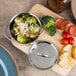 A bowl of food with a lid on a cutting board.