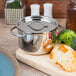 An American Metalcraft stainless steel pot with a lid on a cutting board with bread and broccoli.