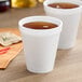 Two Dart white foam cups filled with brown liquid on a table.