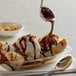 A bowl of ice cream with bananas and Phillips Chocolate Syrup on a table with a spoon.