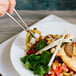 A pair of Town stainless steel chopsticks holding food over a bowl.