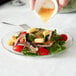 A person pouring dressing onto a salad on an Arcoroc Fleur glass dessert plate.