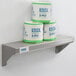 A Lavex stainless steel wall mount shelf with rolls of toilet paper on it.