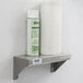 A Lavex stainless steel wall mount shelf holding a spray bottle and paper towel roll.