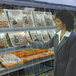 A woman looking at a display of meats through a clear plastic strip curtain.