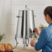 A woman pouring coffee from a stainless steel coffee chafer urn into a glass.