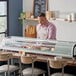 A man in a pink shirt and apron standing behind an Avantco Countertop Refrigerated Sushi Display Case.