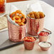 A Choice hammered copper stainless steel round sauce cup filled with red sauce on a table with fried food in copper buckets.