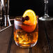A wine glass with a drink, ice cubes, and Fabbri Amarena Cherries with a slice of orange on top.