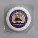 A round white cheese in plastic wrap with a purple label.