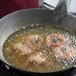 A frying pan of onion rings being fried in cottonseed oil.