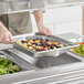 A person using a Vollrath stainless steel hexagon pan to hold fruit and berries on a salad bar counter.