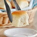 A person using a fork to cut a piece of King's Hawaiian dinner roll on a white plate.