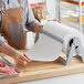 A person in a brown apron using a Choice White Economy Freezer Paper roll to wrap meat.