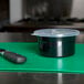 A Carlisle black plastic crock with a lid and a knife on a green cutting board.