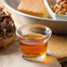 A shot glass of Wright's liquid smoke next to a plate of beans and bread.