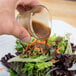 A person pouring Ken's Foods Balsamic Vinaigrette on a salad.