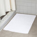 An open white Oxford bath mat on a white tile floor.