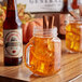 A close up of a Reading Soda Works Pumpkin Spice Soda bottle on a table with a glass mug filled with orange liquid and cinnamon sticks.