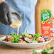 A gloved hand pours Wish-Bone Italian Dressing onto a salad.