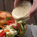 A person pouring Ken's Foods poppyseed dressing onto a bowl of salad.