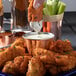 A hand dipping fried chicken into a Choice copper-plated stainless steel sauce cup.
