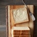 A slice of Harvest Pride wheat bread with butter on a cutting board.