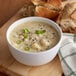 A bowl of Spring Glen Cheesy Potato Soup with green onions and a piece of bread.