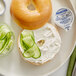 A plate with a bagel topped with Philadelphia cream cheese and cucumber slices.