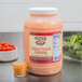 A large plastic container of Ken's Foods Deluxe French Dressing on a table with a bowl of lettuce.