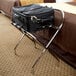 A black suitcase on a Lancaster Table & Seating chrome folding luggage rack.